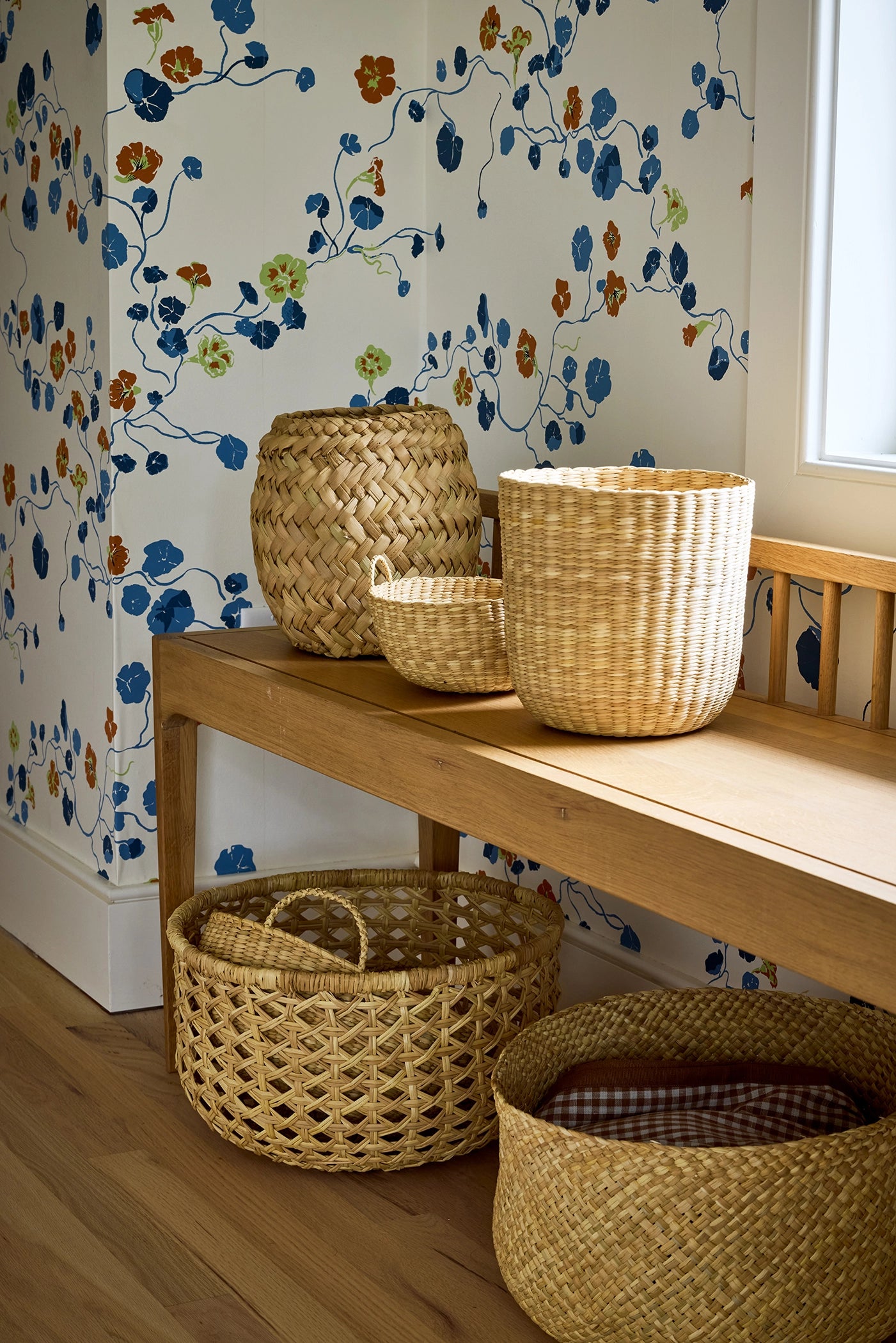 Woven baskets on a wooden bench against floral wallpaper