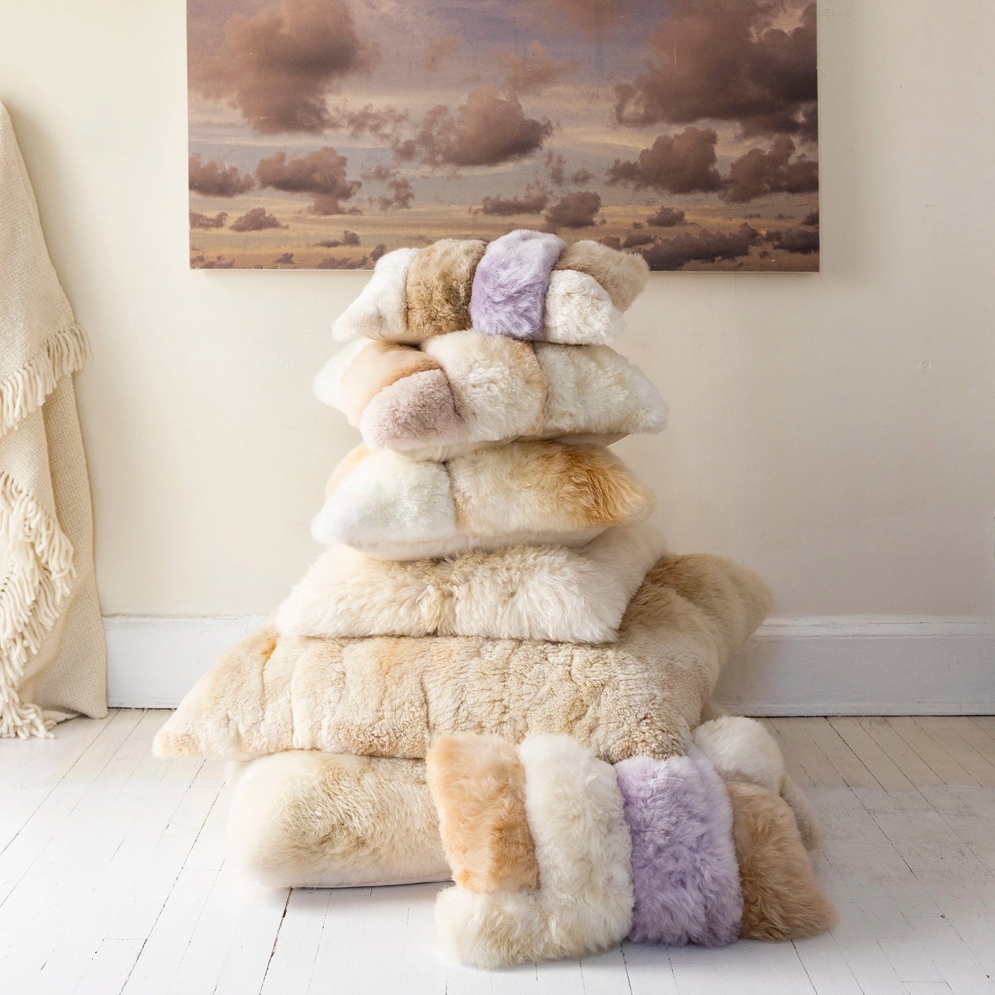 Stack of fluffy alpaca cushions with a painting of a landscape on the wall