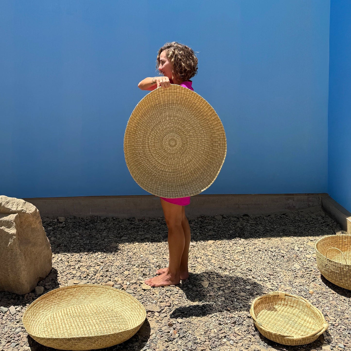 Woman standing in front of blue wall holding oversized basket platter with baskets on ground
