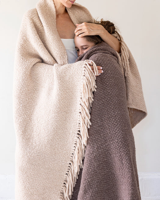 Intiearth Hand loomed throw blanket in rich mineral brown and nude with fringe wrapping mother and daughter