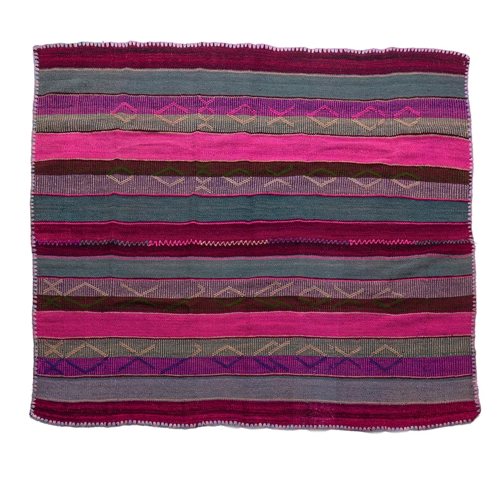 A square woven textile with horizontal stripes in pink, teal, purple, brown, and gray, featuring geometric diamond patterns and a fringed border, shown flat against a white background.