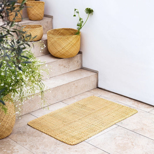 Woven mat on a tiled floor with steps and wicker planters.