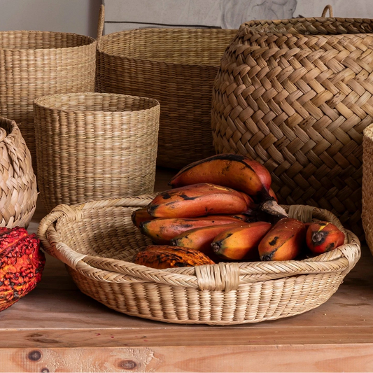 Round wicker basket platter with red bananas on wood table surrounded by baskets