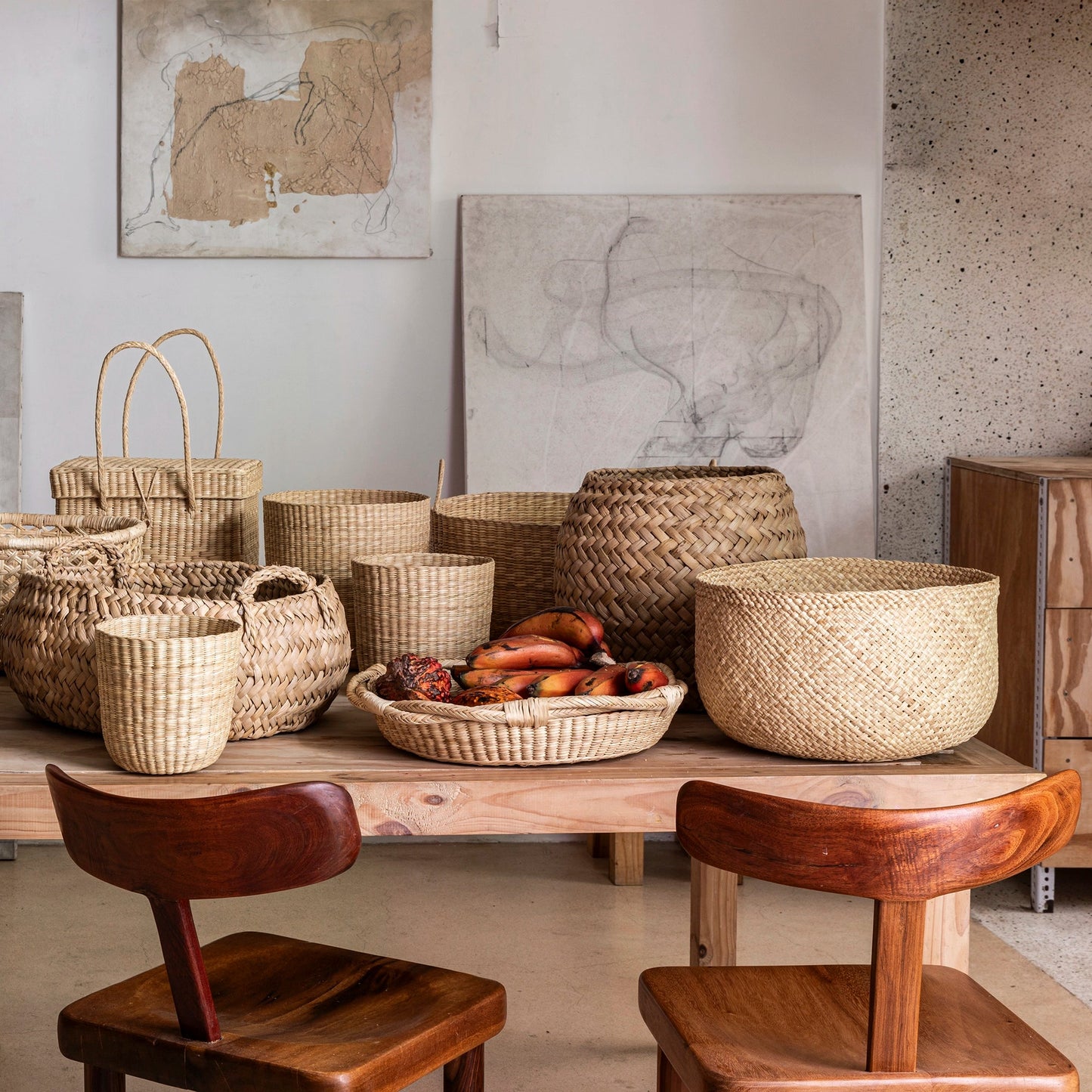 Woven baskets on a wooden table with wooden chairs in a room with abstract art on the wall.
