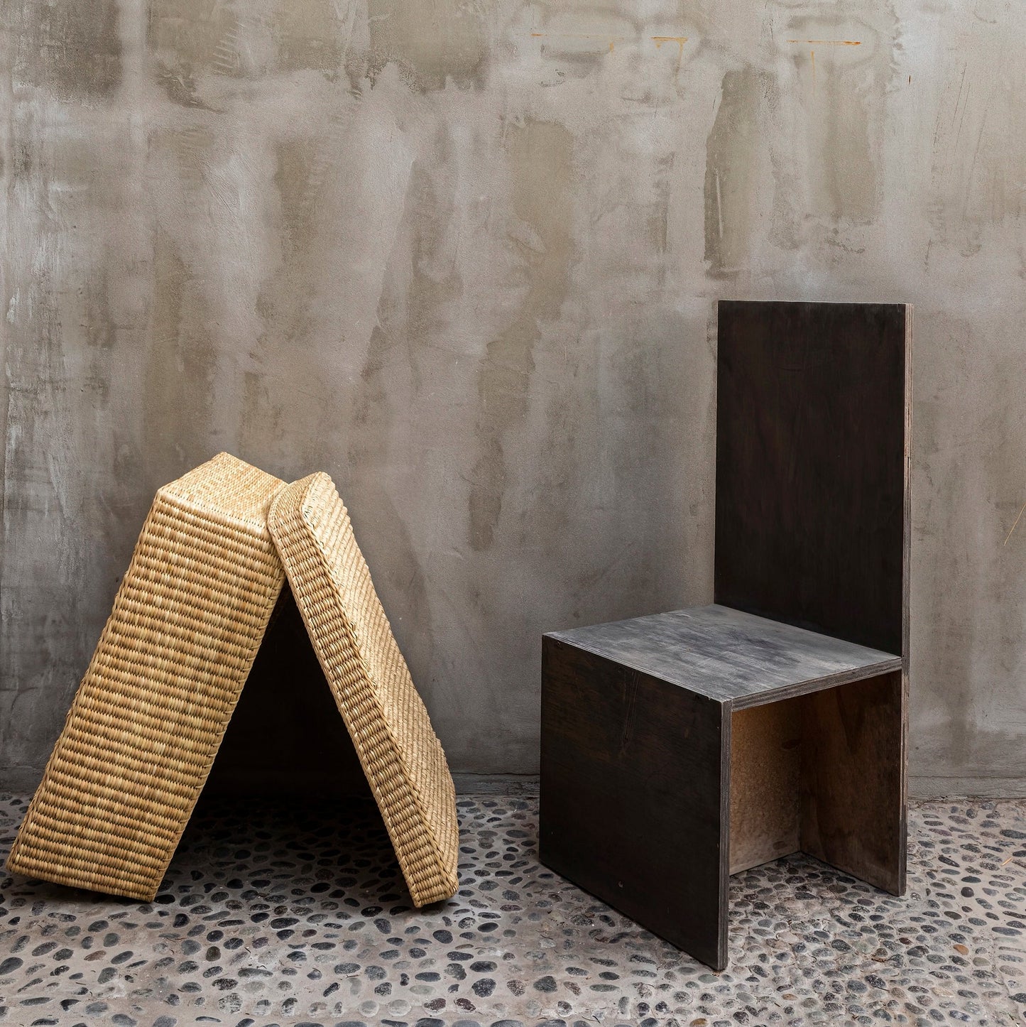 Two unique stools, one woven and one solid, against a textured wall.