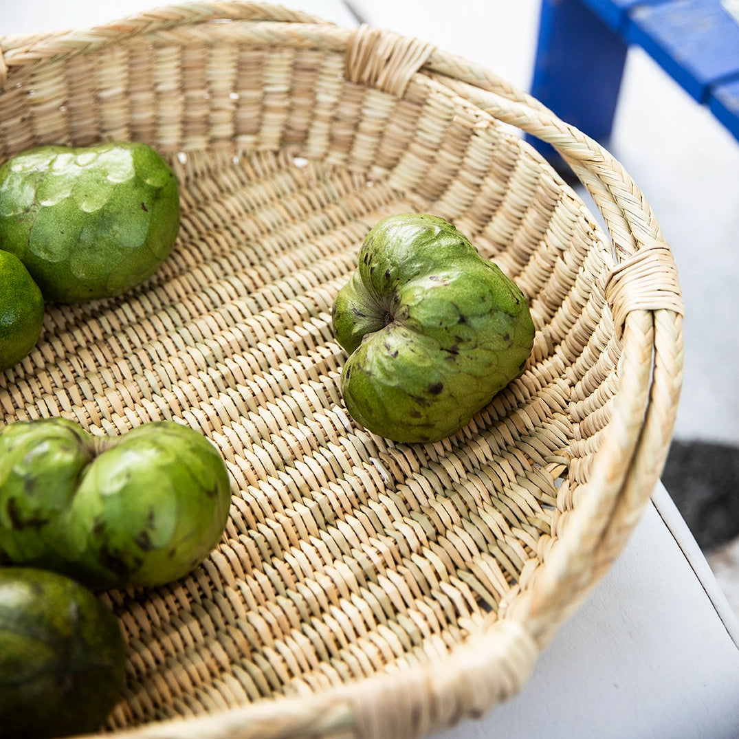 Round wicker basket platter with cherimoya fruit and blue table in background
