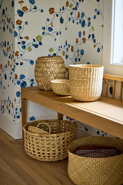 Woven baskets on a wooden bench against floral wallpaper