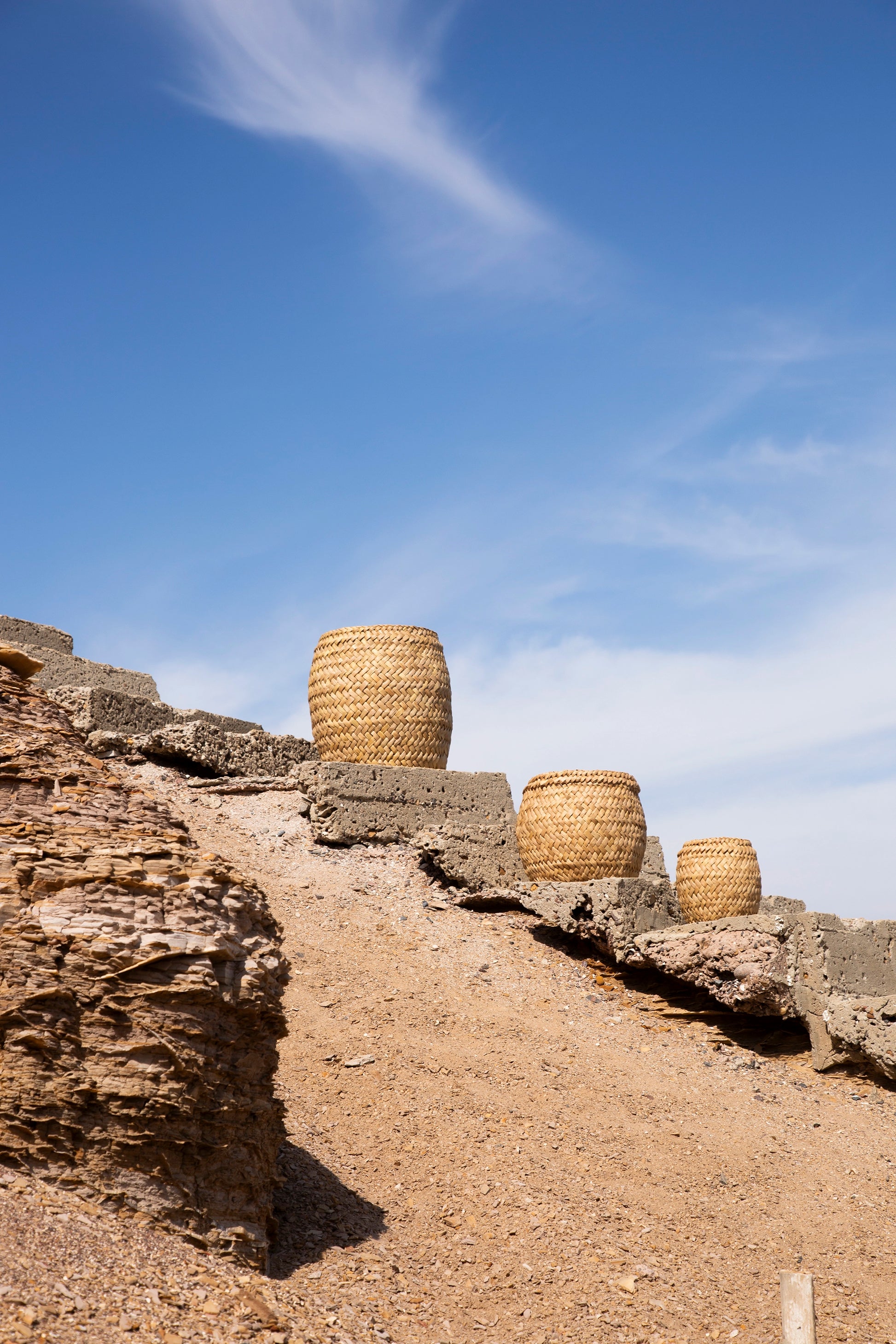 Three woven baskets on a stone ledge against a blue sky with light clouds