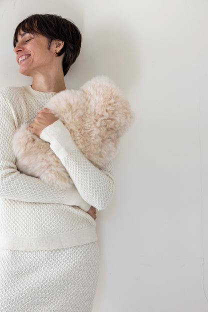 Woman wearing a white textured sweater holding an Intiearth Alpaca Fur Hot Water Bottle Cover in champagne color