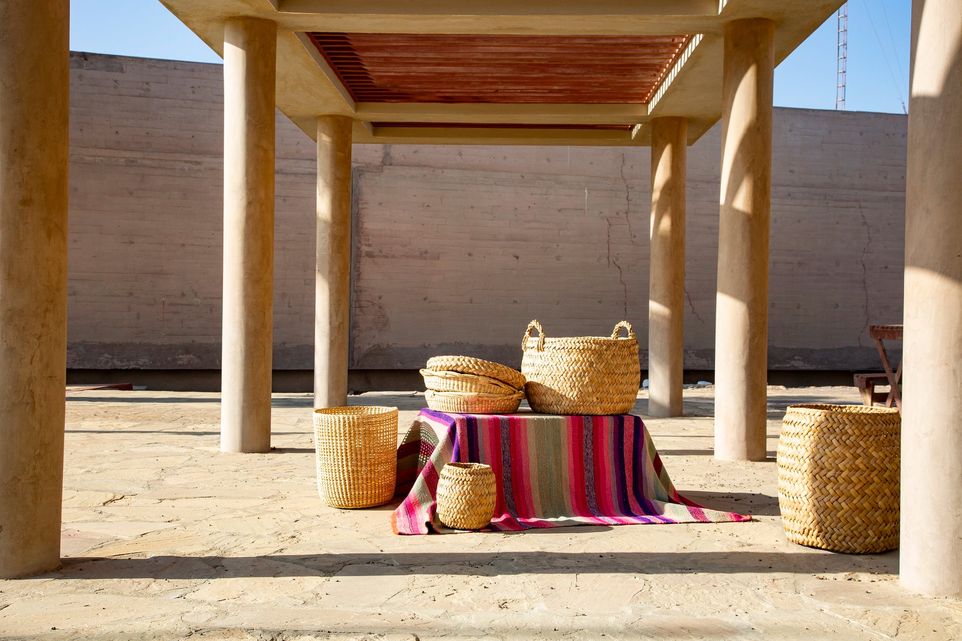 Wicker baskets and a colorful striped blanket on a wooden table under a concrete structure.