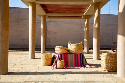 Wicker baskets and a colorful striped blanket on a wooden table under a concrete structure.