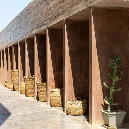 Row of wicker baskets against a stone wall with a cactus plant in the foreground.