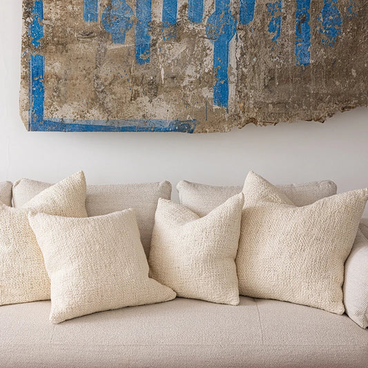 Beige sofa with decorative pillows and a textured wall art piece above it.