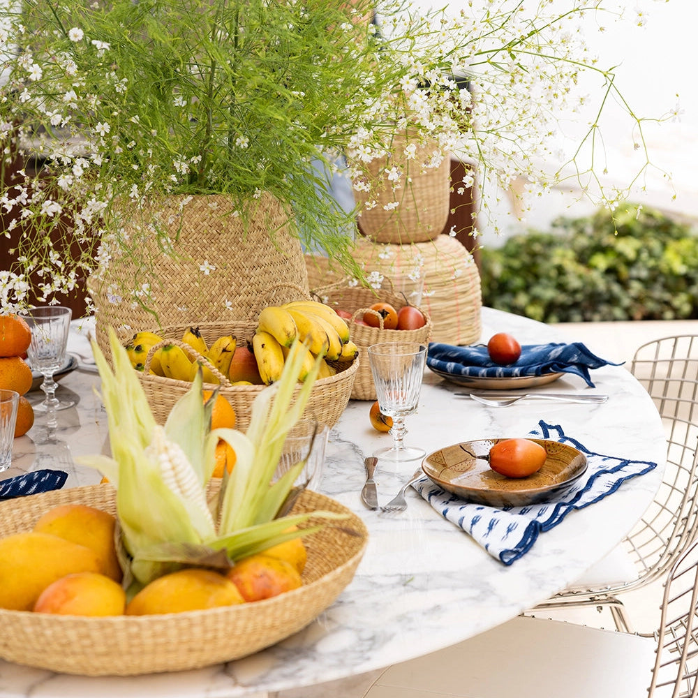 Outdoor setting with a table displaying fruits and flowers in Intiearth baskets surrounded by greenery.