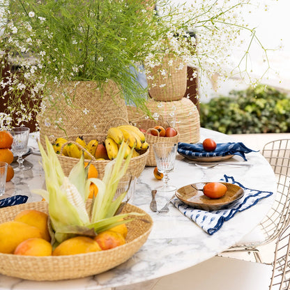 Outdoor setting with a table displaying fruits and flowers in Intiearth baskets surrounded by greenery.