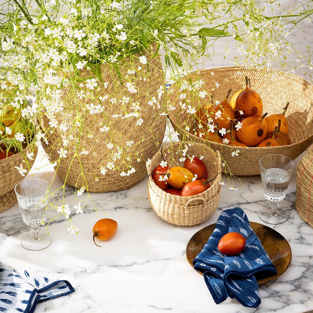 Table setting with wicker baskets, fruits, and flowers on a marble surface.