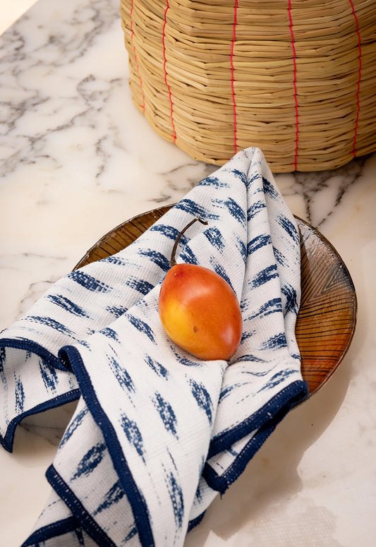 White towel with blue patterns on a marble surface with a basket and fruit.
