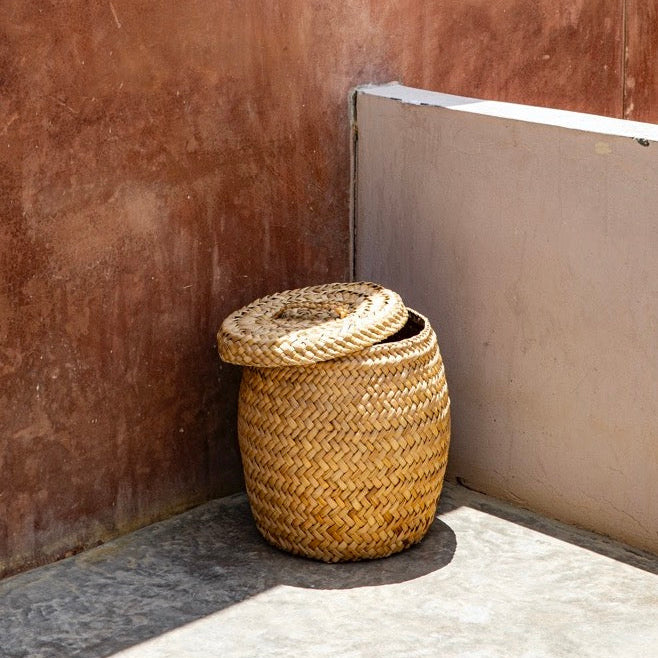 Woven basket with a lid against a textured wall.