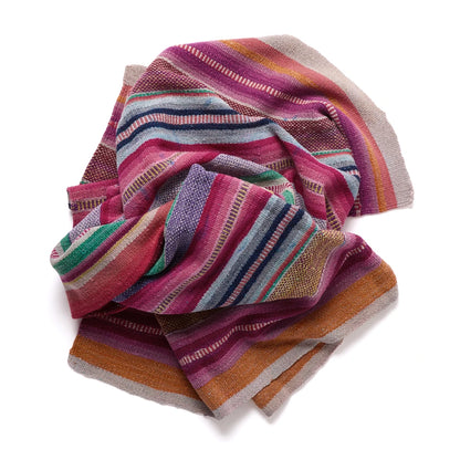 A multicolor striped woven textile, likely a throw blanket or scarf, featuring horizontal bands of pink, purple, orange, green, and blue on a white background.