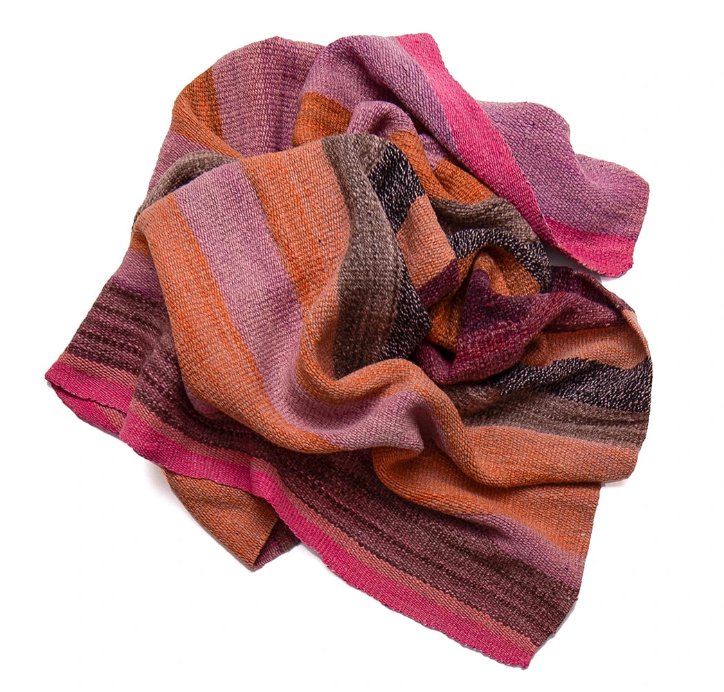 A multicolor striped knit scarf with shades of pink, orange, brown, and purple, styled in soft folds on a white background.