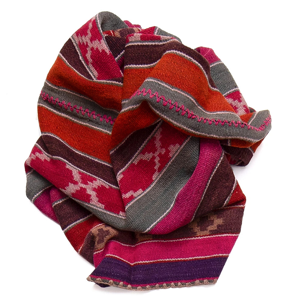 A folded knit blanket or rug with a Southwestern geometric pattern in red, orange, pink, brown, and gray, shown on a solid white background.