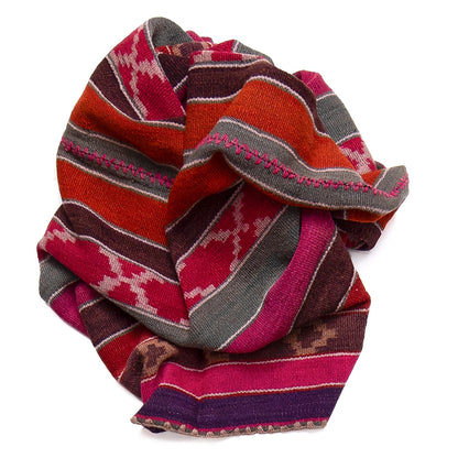 A folded knit blanket or rug with a Southwestern geometric pattern in red, orange, pink, brown, and gray, shown on a solid white background.