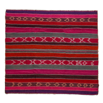 A square woven textile rug with horizontal stripes in pink, red, orange, brown, gray, and purple, featuring geometric diamond and X patterns.