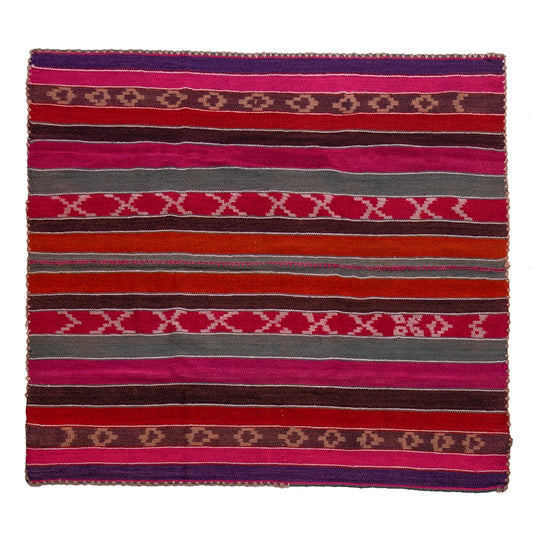 A square woven textile rug with horizontal stripes in pink, red, orange, brown, gray, and purple, featuring geometric diamond and X patterns.
