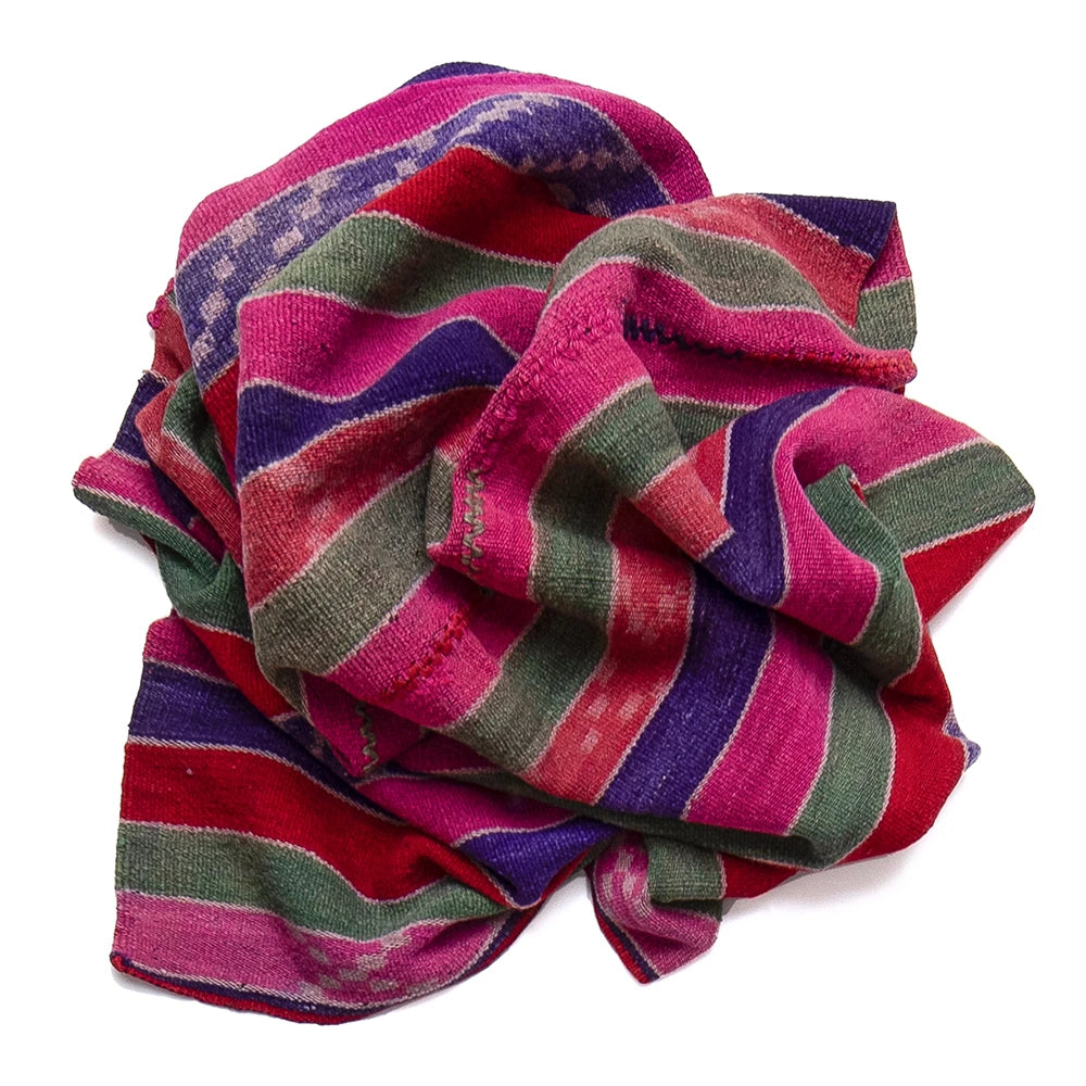 A multicolor striped textile rug with horizontal bands of magenta pink, purple, olive green, and red, styled in a loose, crumpled shape on a white background.