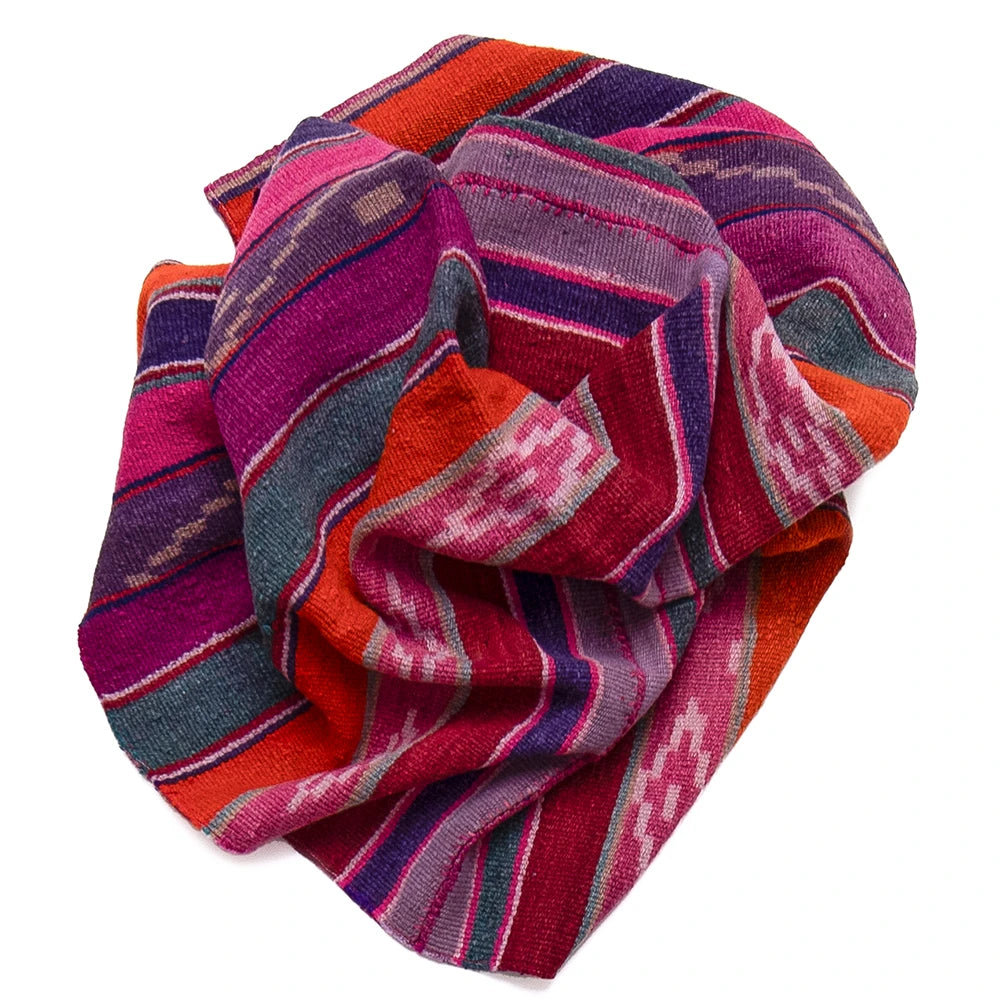A folded multicolor woven textile with bold striped and geometric patterns in red, orange, pink, purple, blue, and gray on a plain white background.