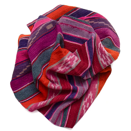 A folded multicolor woven textile with bold striped and geometric patterns in red, orange, pink, purple, blue, and gray on a plain white background.