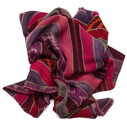 A folded multicolor woven textile with striped and geometric patterns in pink, purple, red, orange, and gray, shown on a plain white background.