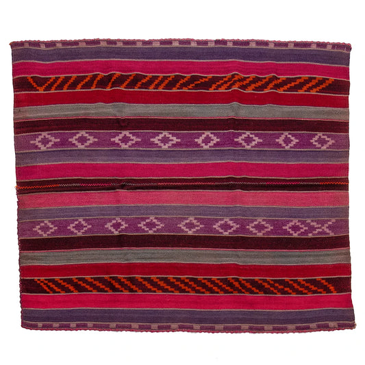 A square woven textile blanket with horizontal stripes and geometric diamond patterns in shades of pink, purple, red, orange, and gray, shown flat against a white background.