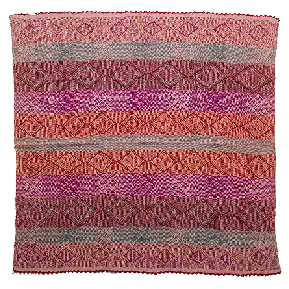 Woven textile with geometric pattern in shades of pink, purple, and red on a white background
