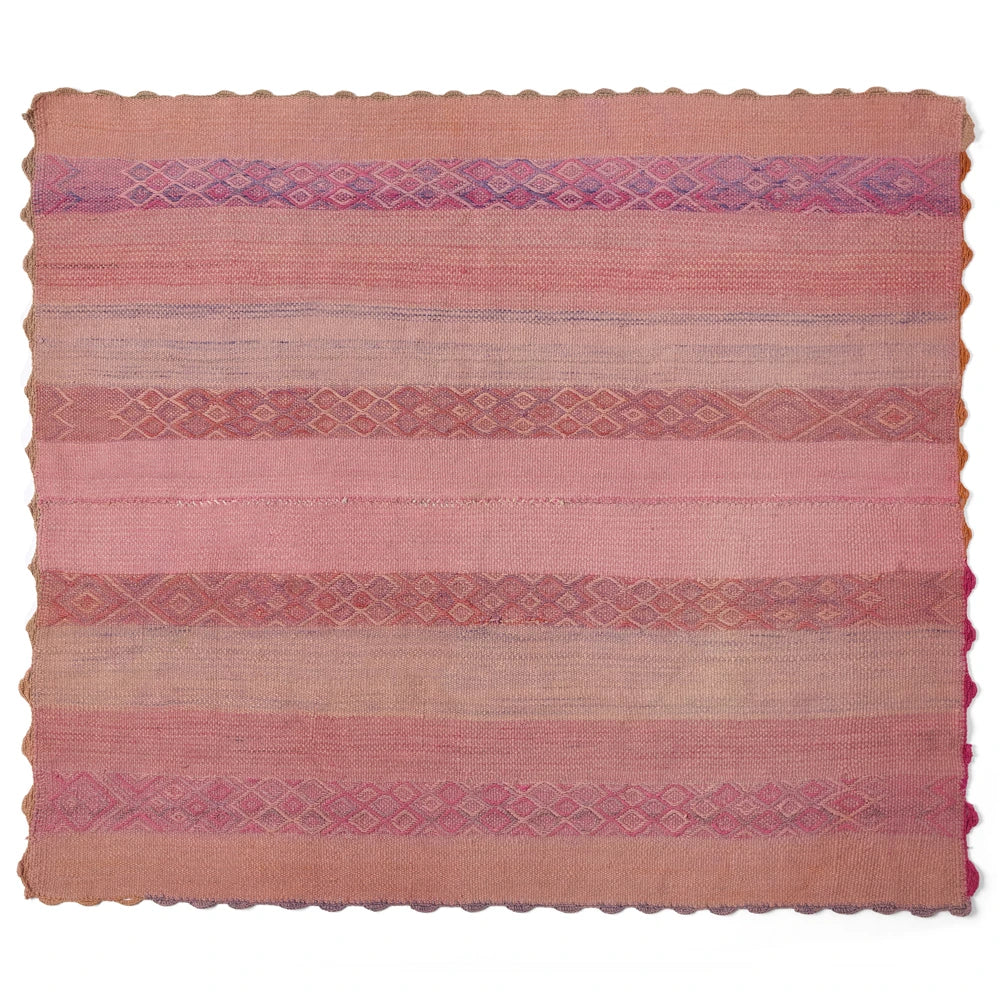 A square handwoven kilim rug in shades of pink, terracotta, and beige, featuring horizontal stripes with diamond and geometric patterns and a scalloped edge.