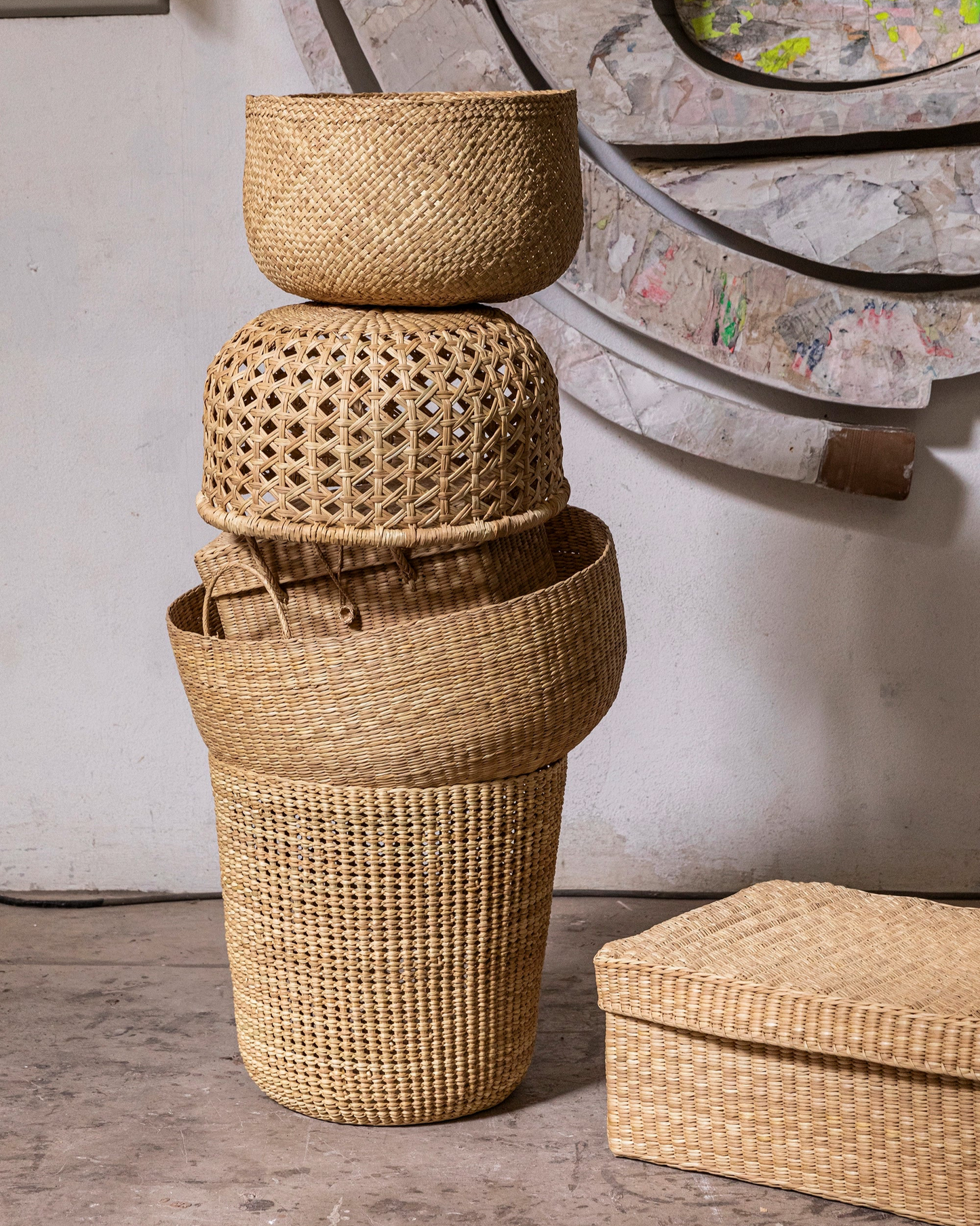 Stack of woven baskets on a wooden floor with a textured wall in the background
