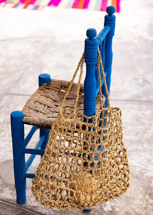 Intiearth Playa woven bag hanging on a blue chair with a colorful striped towel in the background.