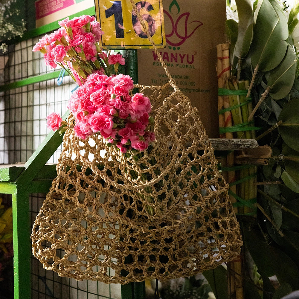 Intiearth Playa woven  bag with pink flowers and a cardboard box labeled '16' in an outdoor setting.