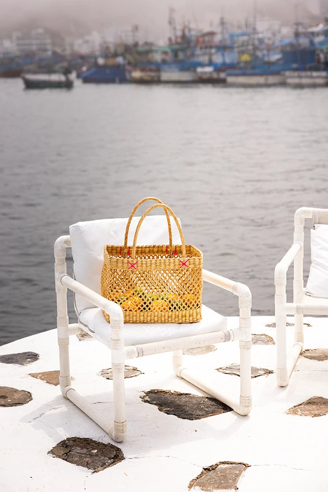 Wicker bag on a white chair by a waterfront with boats in the background