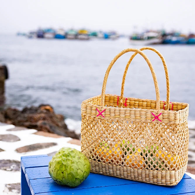 Woven bag with colorful handles on a blue bench by a waterfront