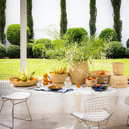 Outdoor setting with a table set for a meal with Intiearth baskets and flowers, surrounded by greenery.