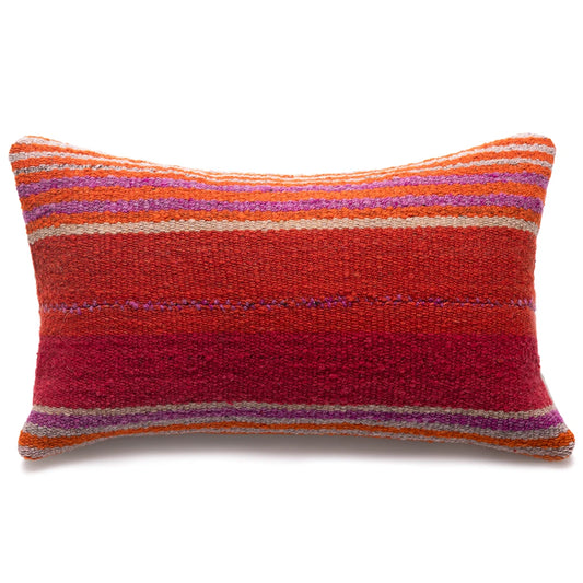 A rectangular handwoven throw pillow with a textured, braided pattern featuring horizontal stripes of red, orange, purple, and beige on a white background.