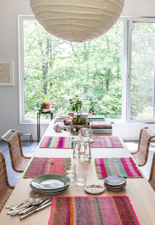 Colorful placemats on a wood table set with glasses and plates for a dinner party