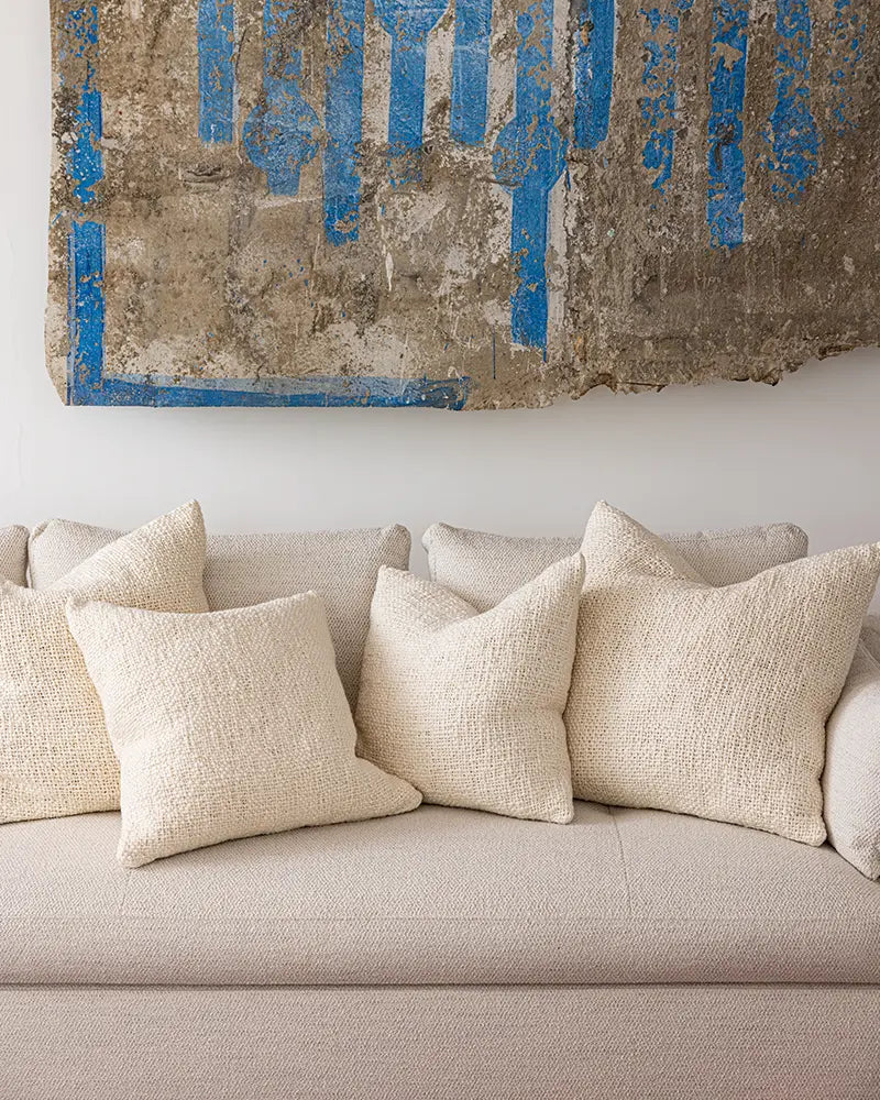 Beige sofa with textured pillows against a wall with abstract blue and brown artwork.